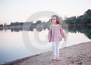 The little stylish girl walks on the bank of the lake. A beautiful portrait of the girl