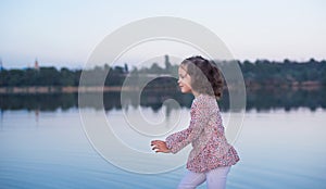 The little stylish girl walks on the bank of the lake. A beautiful portrait of the girl
