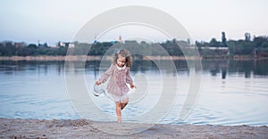 The little stylish girl walks on the bank of the lake. A beautiful portrait of the girl