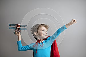 Little superhero boy in a red cape plays with an airplane. Happy smiling child. Success, motivation and travel