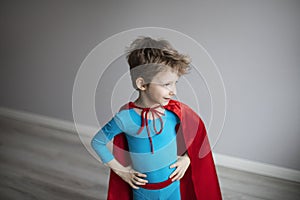 Little superhero boy standing against a gray wall at home