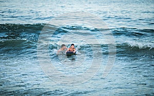 Little surfer learn to ride on surfboard on sea wave. Father with son play in summer ocean, learning surfing. Little boy swim on