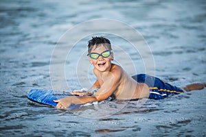 Little surfer learn to ride on surfboard on sea wave. Kid play in summer ocean, learning surfing, riding a wave. Little boy swim