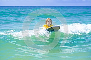 Little surfer learn to ride on surfboard on sea wave. Kid play in summer sea. Kid girl is learning surfing, riding a