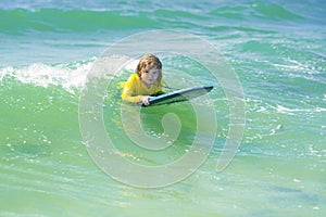 Little surfer learn to ride on surfboard on sea wave. Summer vacation with child. Kid girl is learning surfing, riding a