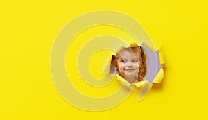Little surprised child looking, peeping through the bright yellow paper hole. Advertise childrens goods. Happy childhood concept.