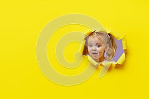 Little surprised child looking, peeping through the bright yellow paper hole. Advertise childrens goods. Happy childhood concept.