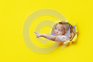 Little surprised child looking, peeping through the bright yellow paper hole. Showing hand to side. Advertise childrens goods.