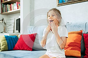 Little surprised teen girl watching tv at home.