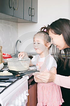 Little sweet girl and her mother fry pancakes at the traditional Russian holiday Carnival Maslenitsa Shrovetide