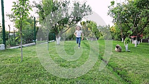 A little sweet girl runs along the green grass with her friend the dog. friendship between child and animal. Slow motion.