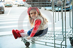 A little sweet girl is sitting in a supermarket shopping cart.
