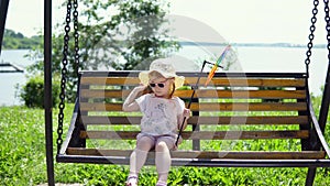 A little sweet girl in sunglasses swings on a seesaw on a sunny warm day.