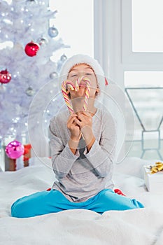 Little sweettooth boy holds delicious candies in front of mouth, looks directly at camera,  over white new year