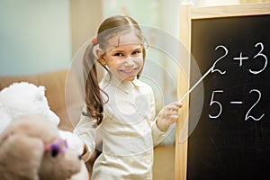 Little teacher. Beautiful young girl is teaching toys at home on blackboard.