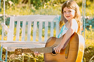 Little teen girl musician playing guitar. Dreamy kids face. Smiling child playing outdoors in summer.