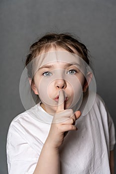 Little teenage girl holding her finger to her mouth showing a sign of silence.
