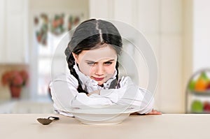 little teenage girl sitting at the dining table in the kitchen. Doesn\'t eat healthy food. No appetite