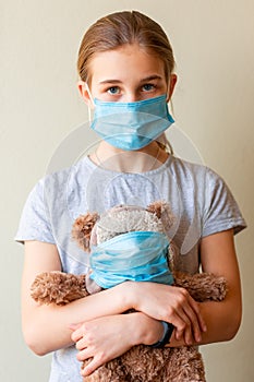 Little teenage girl with teddy bear toy both in medical masks sad and scared
