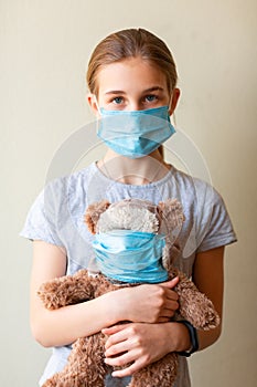 Little teenage girl with teddy bear toy both in medical masks sad and scared