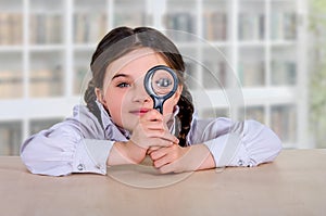 A little teenage schoolgirl girl sits at a table with an optical magnifier. Does homework and studies