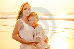 Little teenager cute girl and young mother at tropical beach enjoying the sunset on the sea tenderness and intimacy care