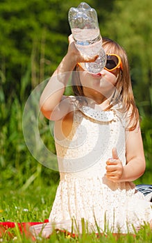 Little thirsty girl child drink water from plastic bottle, outdoor