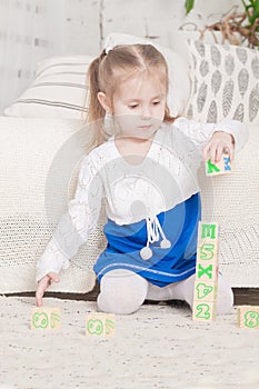 A little three-year-old girl plays cubes on which letters and numbers are drawn