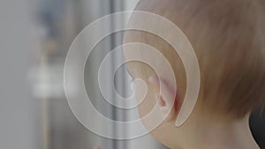 little toddler baby boy lonely looking through window outside. close-up face