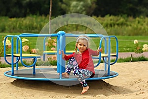 Little toddler barefoot girl in red circling around on a carousel on playground
