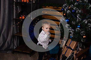 little toddler blonde boy near christmas tree in dark loft room with blue decoration. happy new year