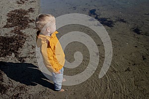 A little toddler boy on the beach wearing yellow jacket