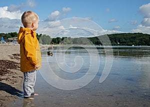 A little toddler boy on the beach wearing yellow jacket, cloudy weather with sunshine