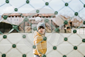 Little toddler boy behind net outdoors, isolated alone during quarantine period at pandemic