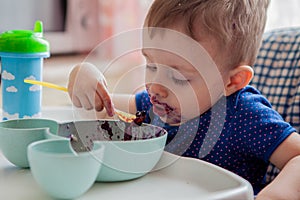 Little toddler boy with dirty face eating fresh blueberry indoor