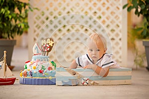 Little toddler boy, dressed as sailor, celebrating his first birthday with sea theme cake, boat, fishes and aqua animals