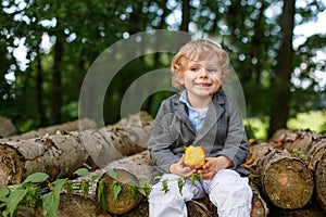 Little toddler boy eating apple in summer forest
