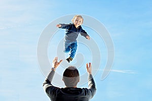 Little toddler boy, flying in the sky, dad throwing him high in the air. Family, enjoying winter view of snowy mountains and