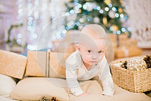 Little toddler boy at home at the Christmas tree with gifts and toys.