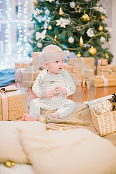 Little toddler boy at home at the Christmas tree with gifts and toys.