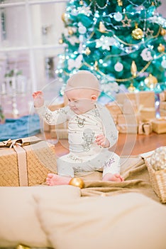 Little toddler boy at home at the Christmas tree with gifts and toys.