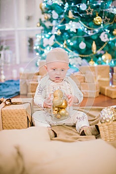 Little toddler boy at home at the Christmas tree with gifts and toys.