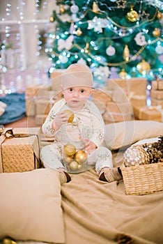 Little toddler boy at home at the Christmas tree with gifts and toys.