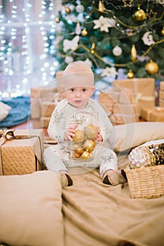 Little toddler boy at home at the Christmas tree with gifts and toys.