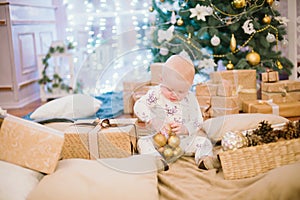 Little toddler boy at home at the Christmas tree with gifts and toys.