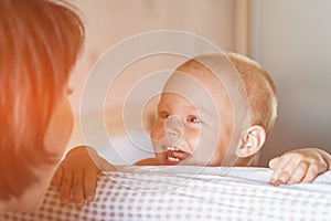 Little toddler boy playing on the bed. Cute kid smiling and hiding under cover. Palyful and mischievous eyes. Hide-and-seek.