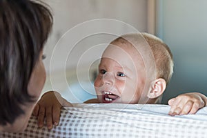 Little toddler boy playing on the bed. Cute kid smiling and hiding under cover. Palyful and mischievous eyes. Hide-and-seek.