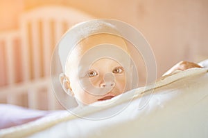 Little toddler boy playing on the bed. Cute kid smiling and hiding under cover. Palyful and mischievous eyes. Hide-and-seek.