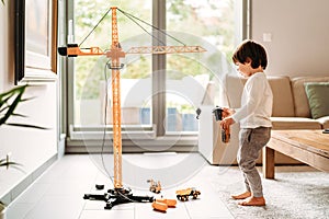 Little toddler boy playing with big construction building crane toy at home in living room.