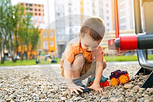 Little toddler boy playing with cars on pebbles on the playground.